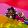 Person wearing headphones and colorful shirt, smiling and enjoying music, set against a vibrant, multicolored background, reflecting a festive atmosphere suitable for party events.